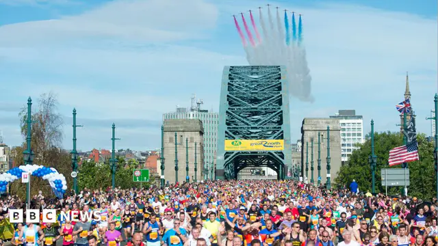 Crowds of runners, wearing colourful tops, run across the Tyne Bridge. A set of planes (Red Arrows) can been in the blue sky, leaving a trail of white, red and blue markings in the sky.