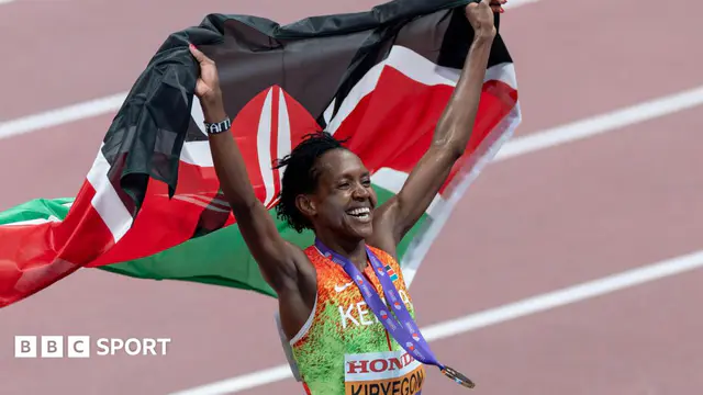 Faith Kipyegon, wearing an orange and green Kenyan athletics vest, with a gold medal on a purple ribbon bouncing around her neck, smiles broadly as she holds a Kenyan flag aloft behind her. The runner is visible from sto