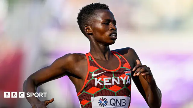 Naomi Korir pictured from stomach up running from left to right during a race. She wears a Kenya running vest made of up light and dark red diamond and chevron patterns with thin green grid lines running over the top and