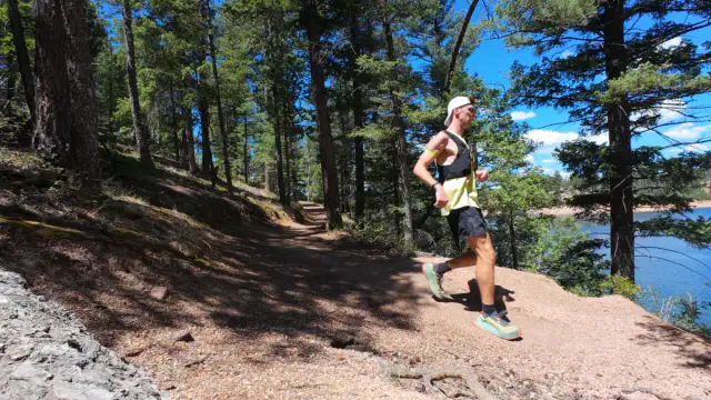 Runner on the Rampart Reservoir trail with singletrack cutting through ponderosa pines above the shoreline