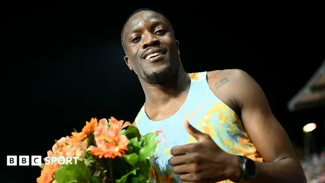 Letsile Tebogo, wearing a predominantly light blue running vest, holds a bouquet of flowers and gives a thumbs up gesture to the camera